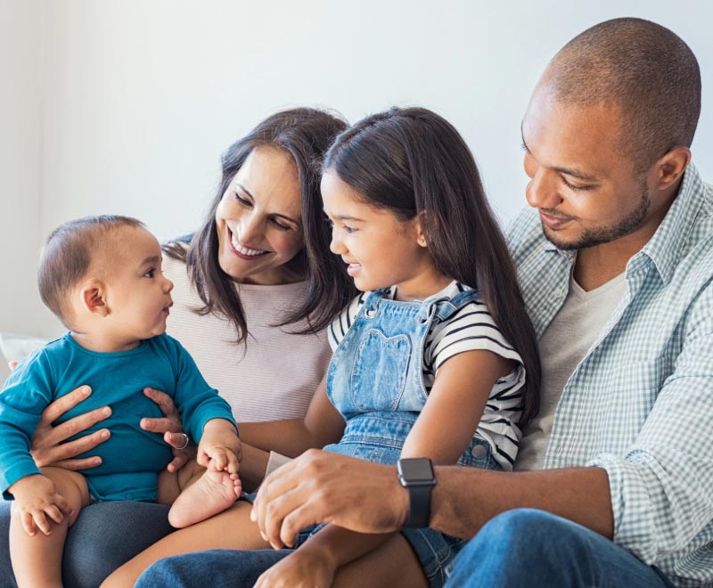 Baby and young child sitting on parent's lap all smiling at each other